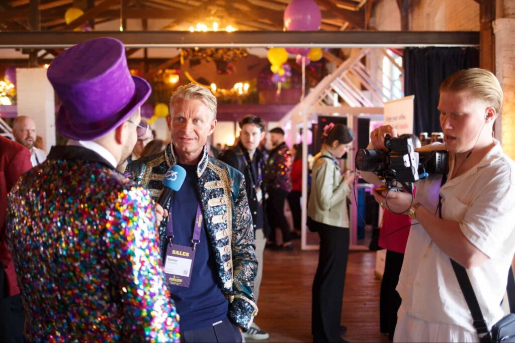 Stefan Smulders conducts an on-camera interview surrounded by event attendees and vibrant decor